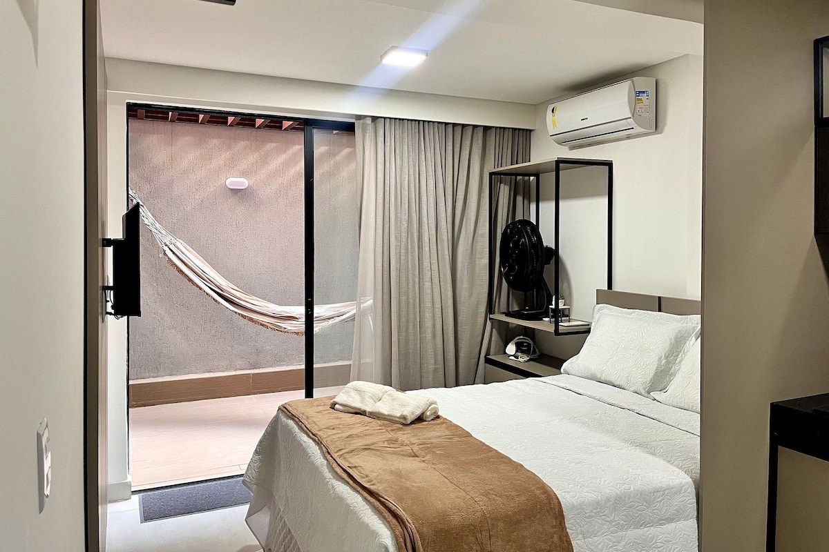 A hotel room with a bed, a nightstand, an air conditioning unit, a mirror, and a sliding glass door leading to a balcony.