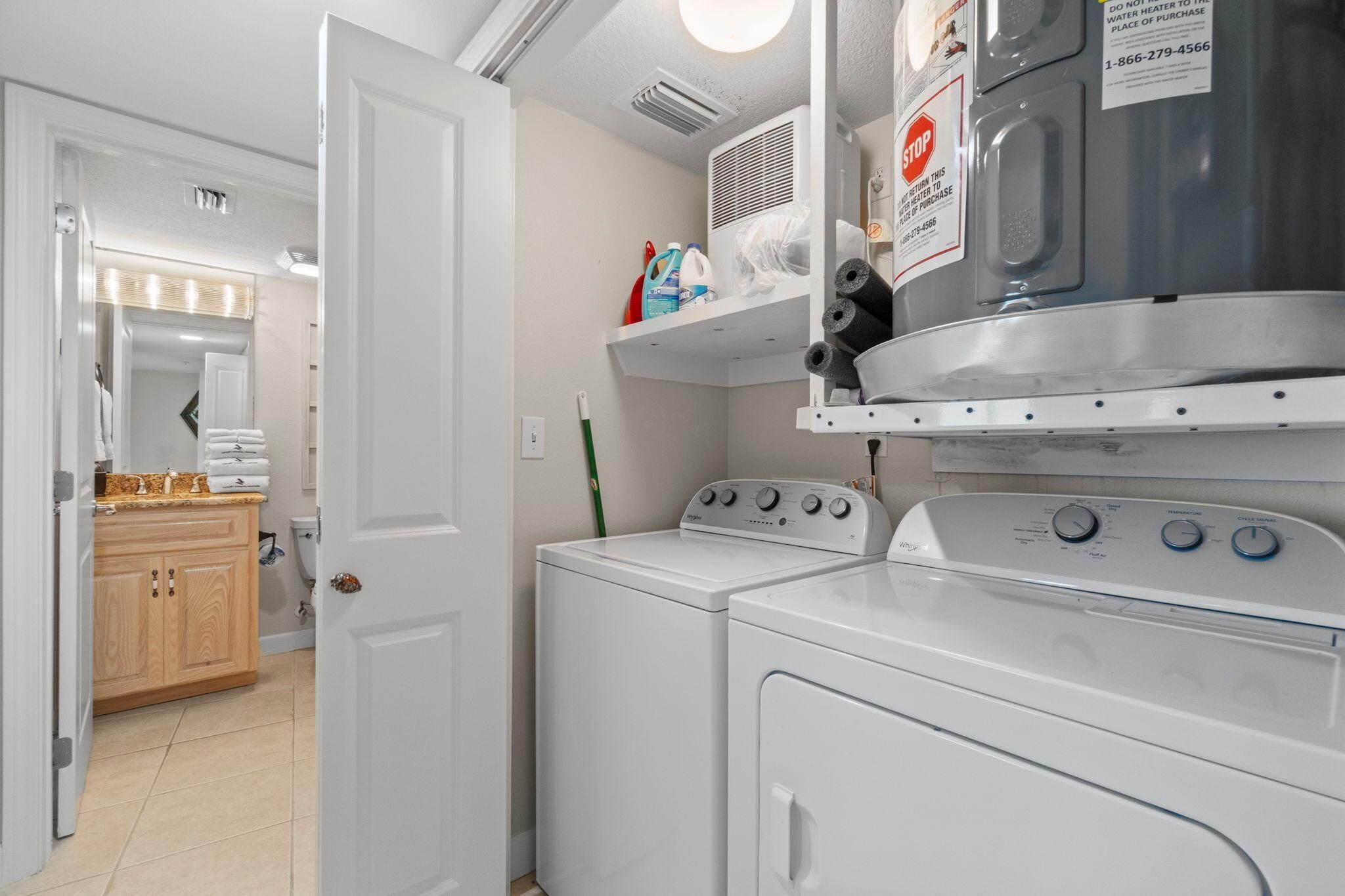 A laundry area with a washer and dryer, a shelf with cleaning supplies, and a door leading to a bathroom.
