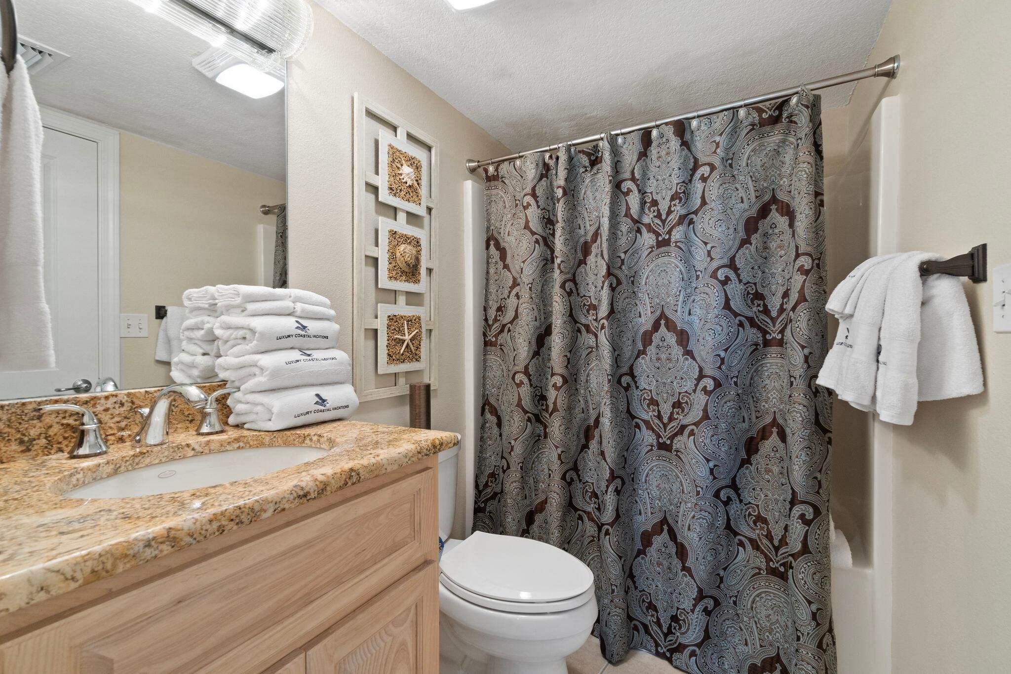 A bathroom with a granite countertop sink, a toilet, and a shower curtain with a paisley pattern.
