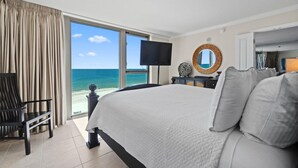 Une chambre d’hôtel avec un grand lit, une télévision, une vue sur la plage et un fauteuil.