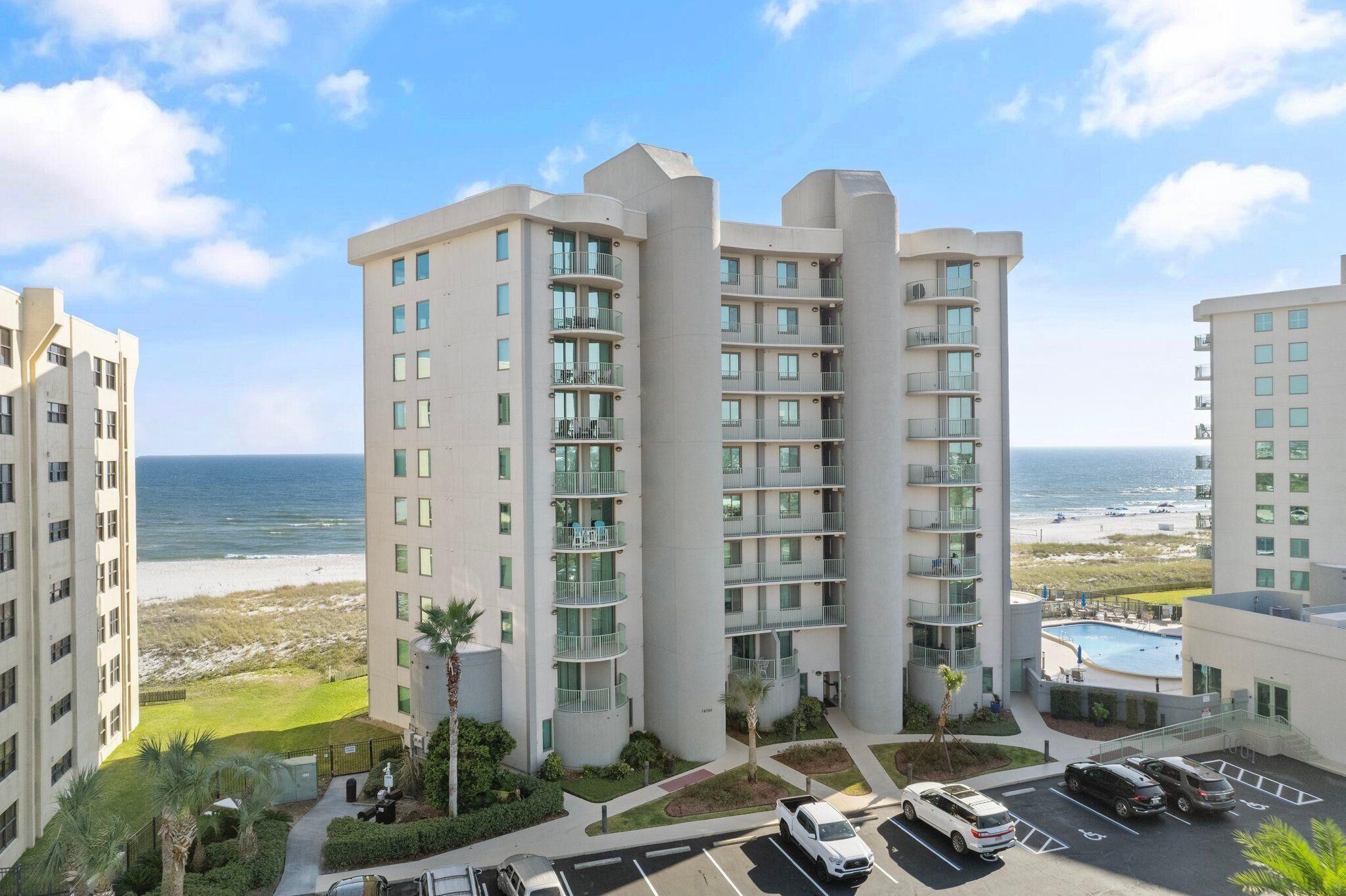 A multi-story hotel with balconies, a swimming pool, and a view of the beach.