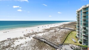 Un hôtel situé en bord de mer, avec une promenade qui mène à la plage, une zone de plage de sable et une vue sur l’océan.