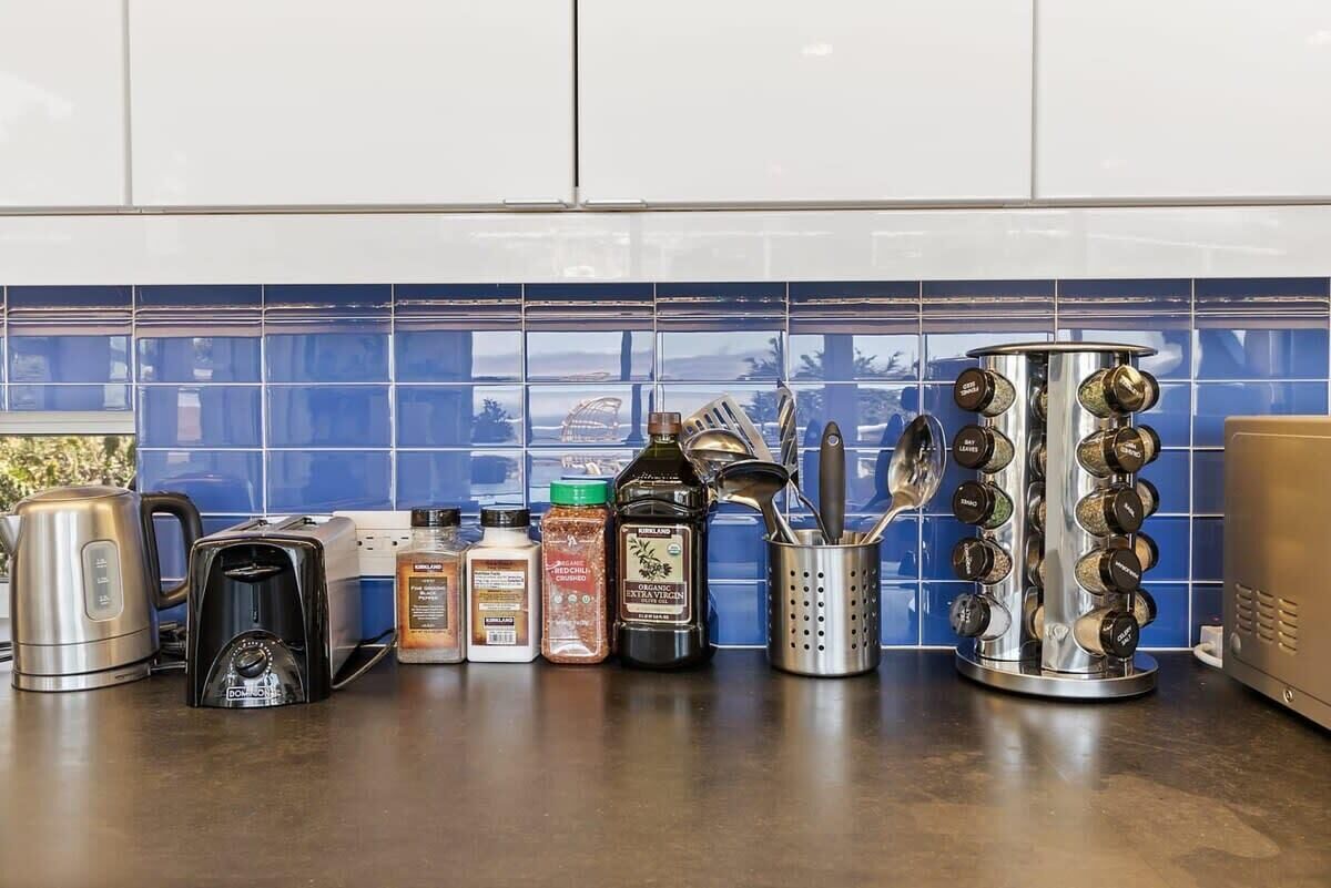 En køkkenbordplade med forskellige køkkenapparater og redskaber, herunder kaffemaskine, brødrister og krydderihylde.