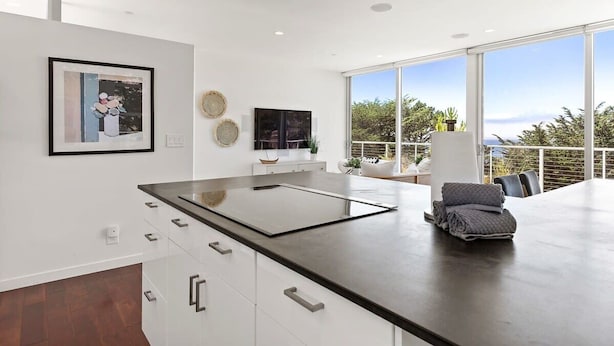 Una cocina moderna con una isla grande, armarios blancos y vistas al exterior a través de amplios ventanales.