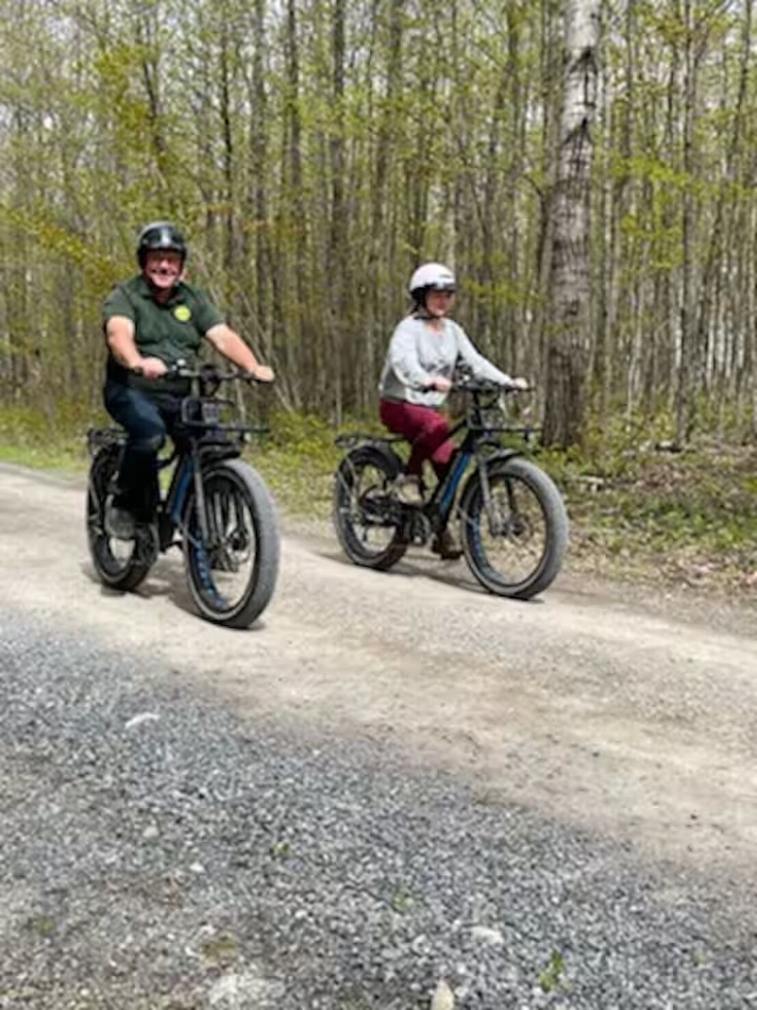 Twee personen fietsen op een grindpad, omringd door bomen.