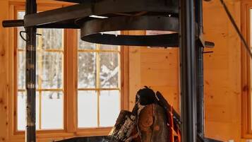 Una estufa de leña con chimenea, ubicada en una habitación con paredes y ventanas de madera.