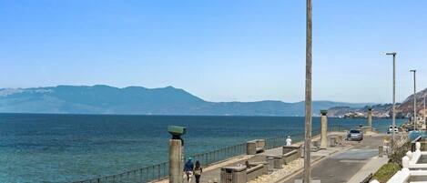 A coastal promenade with a clear view of the sea and mountains in the distance.