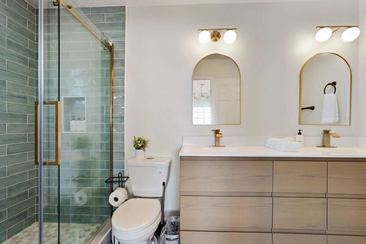 A modern bathroom with a glass shower enclosure, a toilet, a sink with a vanity, and two wall-mounted mirrors.