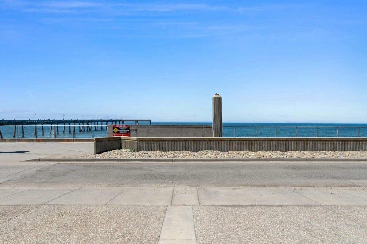 Eine Küstenpromenade mit einer Betonbarriere, Kies und einem entfernten Steg.