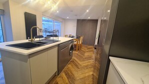 A modern kitchen with a built-in washing machine, a large window, and a dining area with a wooden table and chairs. - 5 Bed Sleeps 10 Full Kitchen Parking (South Ayrshire Council)