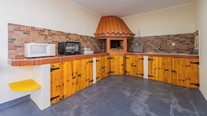 A kitchen with a microwave, toaster, and oven, wooden cabinets, and a tiled backsplash. - Simões Apartment by HR Madeira (Porto Santo)
