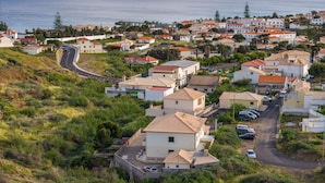 A coastal residential area with houses, a curved road, and a view of the sea. - Simões Apartment by HR Madeira (Porto Santo)