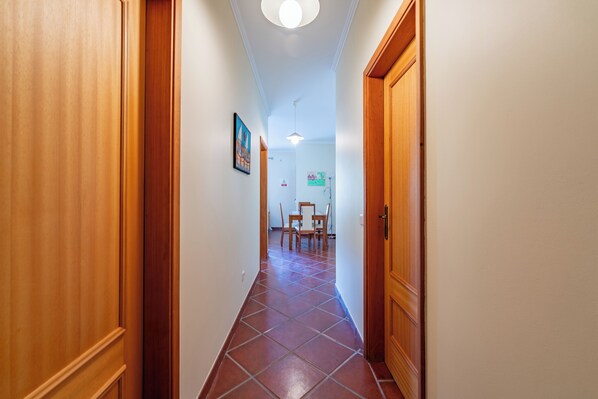 A hallway with wooden doors, a tiled floor, and a dining area with chairs and a table in the distance. - Simões Apartment by HR Madeira (Porto Santo)