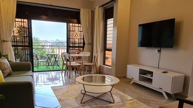 A modern living room with a sofa, a round coffee table, a TV mounted on the wall, and a balcony with a view. - BLT Apartments - classy (Kira Town)
