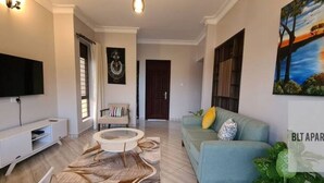 A modern living room with a flat-screen TV, a sofa, a coffee table, and a painting on the wall. - BLT Apartments - classy (Kira Town)