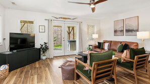 Ein modernes Wohnzimmer mit Flachbildfernseher, Holzboden, Ledersofa, grünen Sesseln und Deckenventilator.