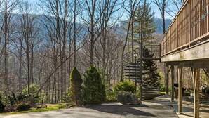 Eine Holzterrasse mit Wendeltreppe, umgeben von Bäumen und einem klaren Himmel.