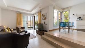 A modern living room with a sofa, TV, and dining area with chairs. - Villa With Heated Pool in Salobre (San Bartolomé de Tirajana)