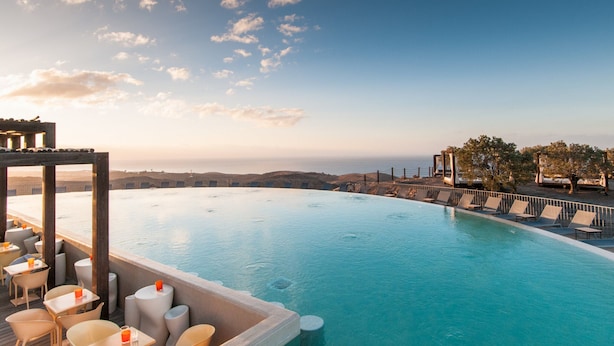 An infinity pool with a view of the ocean and hills, surrounded by lounge chairs and tables. - Villa With Heated Pool in Salobre (San Bartolomé de Tirajana)