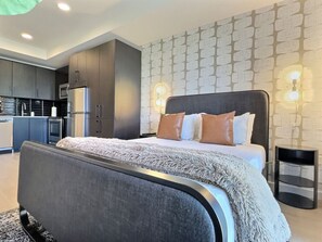 A modern bedroom with a large bed, a built-in wardrobe, and a kitchen in the background. - Stylish Studio, Walk to Food, Bars and Baseball (Birmingham)