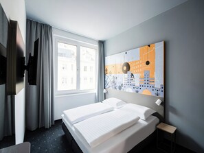 Habitación de hotel con cama, ventana con cortinas, televisor de montaje en pared y una obra de arte con vista a la ciudad.