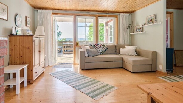 Een gezellige woonkamer met een houten plafond, een grijze bank en een houten kast.