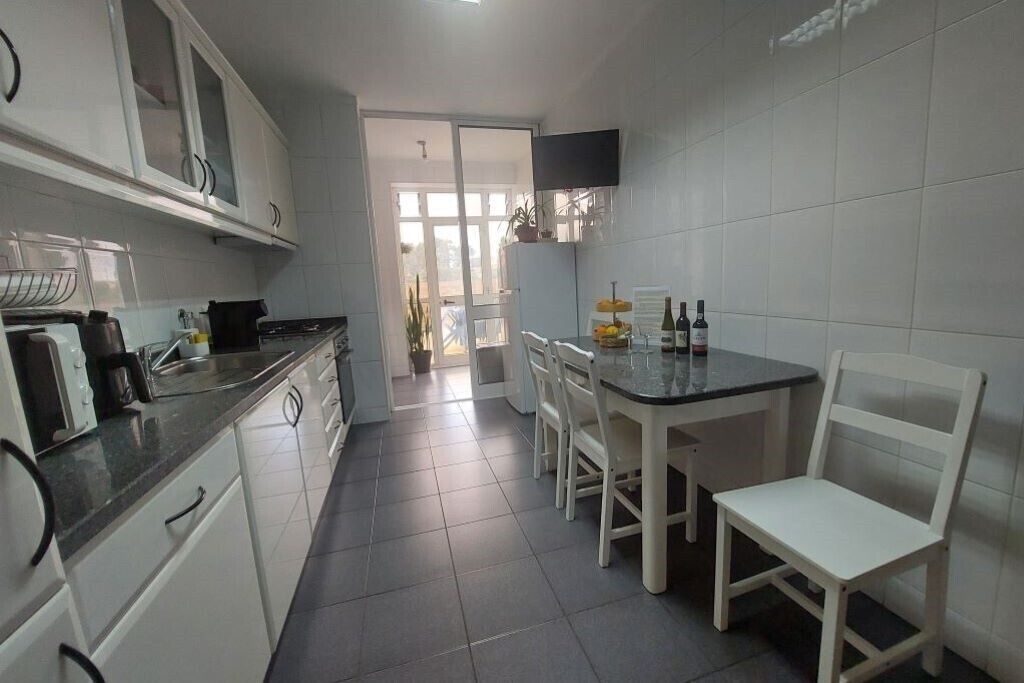 A compact kitchen with white cabinets, a black countertop, and a dining area with a table and chairs.