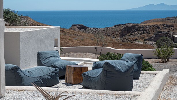 A terrace with outdoor seating, a view of the sea, and rocky terrain. - Villa Chora (Santorini)