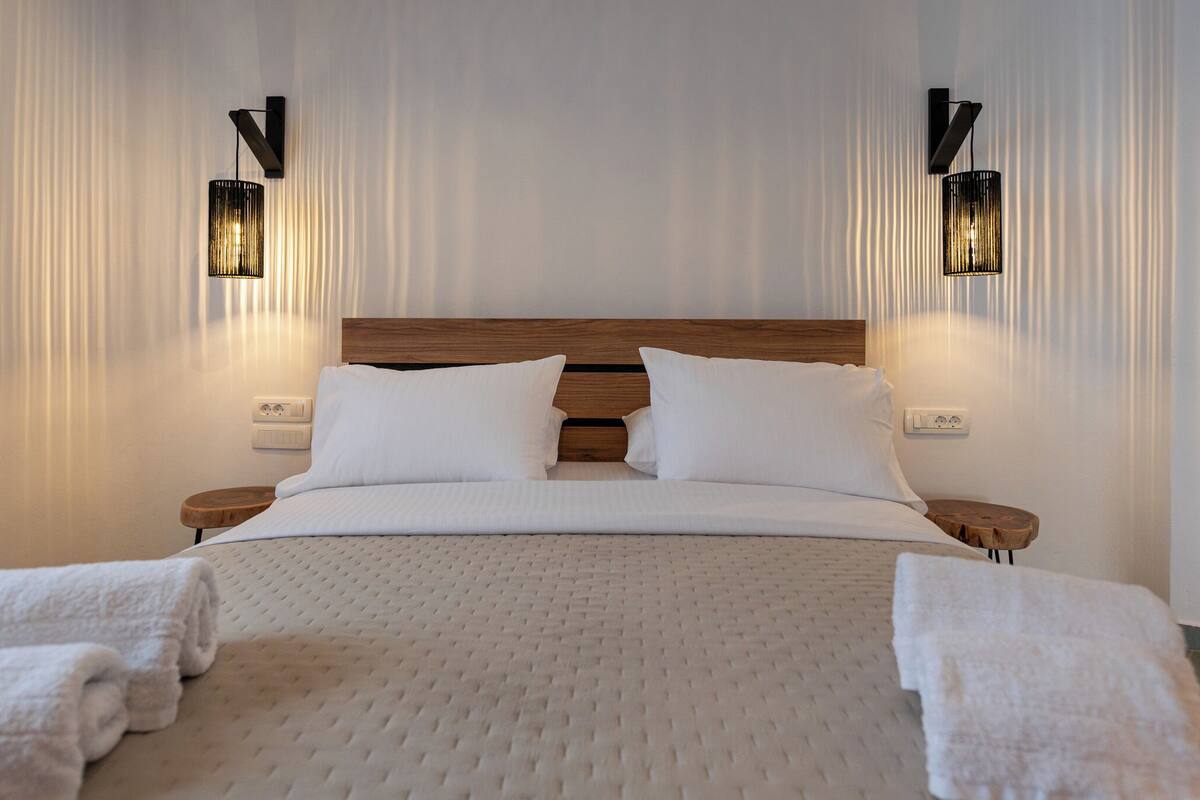 A neatly made bed with white linens, two bedside tables, and wall-mounted lighting fixtures.