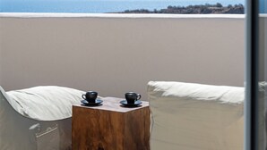 A balcony with a wooden table, two chairs, and a view of the sea and distant mountains. - Villa Chora (Santorini)