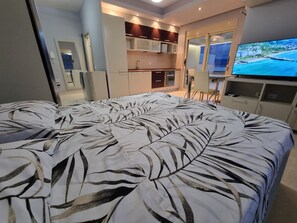 Habitación de hotel moderna con una cama grande, televisión, kitchenette y balcón con vistas.