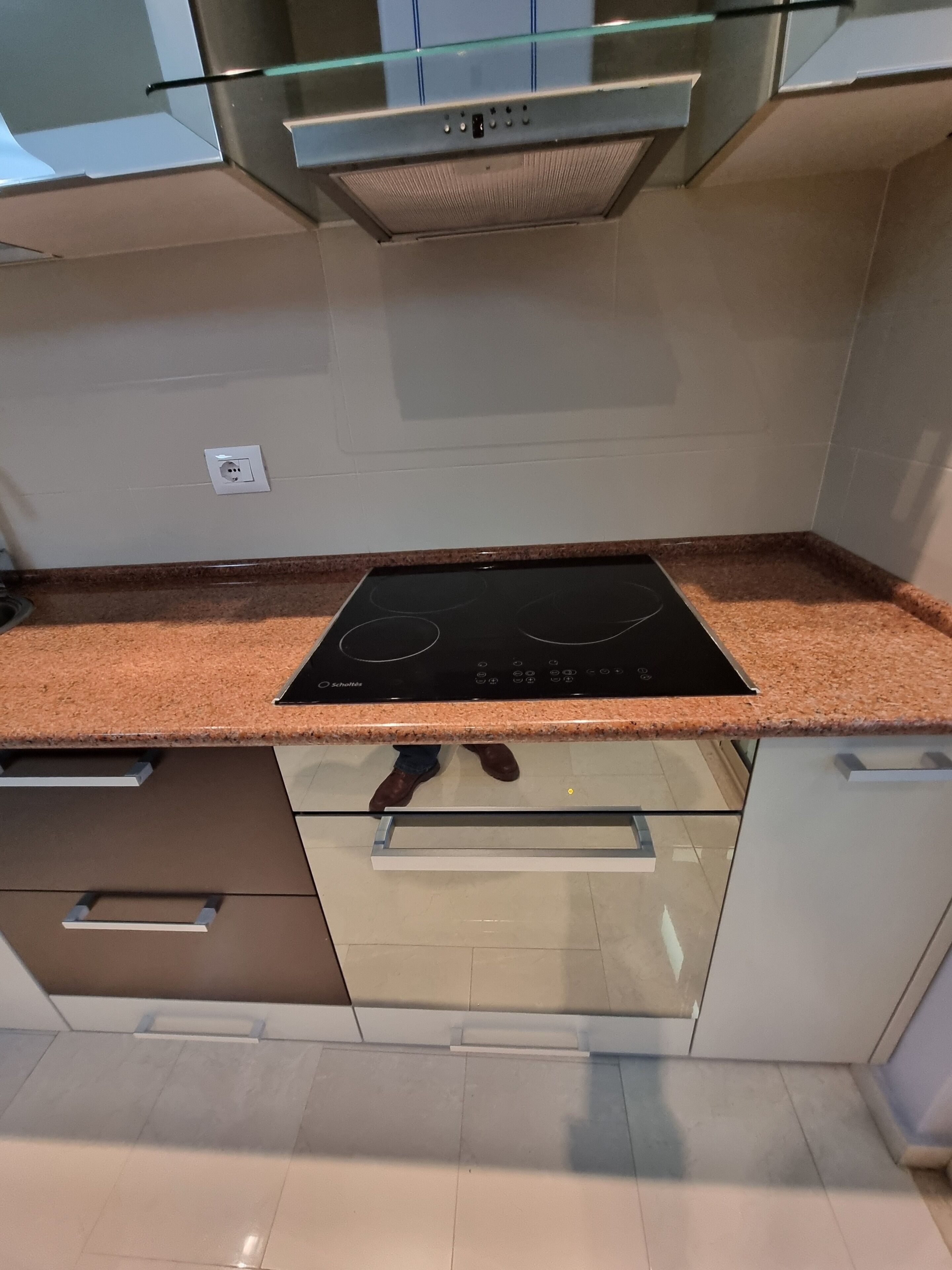 Eine Küche mit einem schwarzen Induktionskochfeld, Edelstahl-Schränken und einer Glasrückwand.