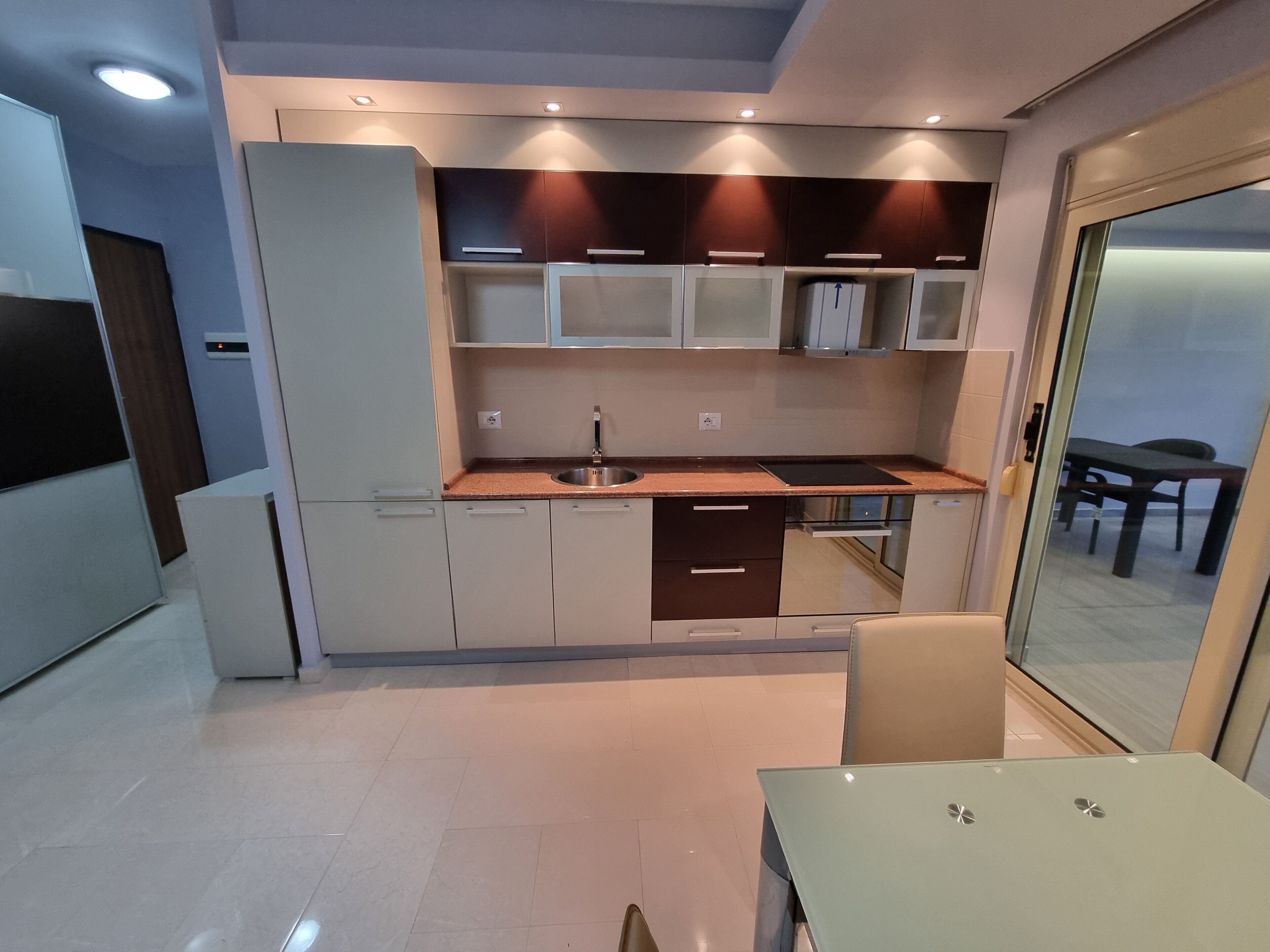 A modern kitchen with built-in appliances, a dining area with a table and chairs, and a large window providing a view.