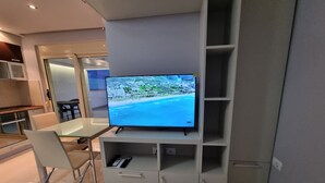 Un salon moderne avec un téléviseur à écran plat fixé sur un meuble de rangement blanc, une table à manger en verre et un canapé blanc.