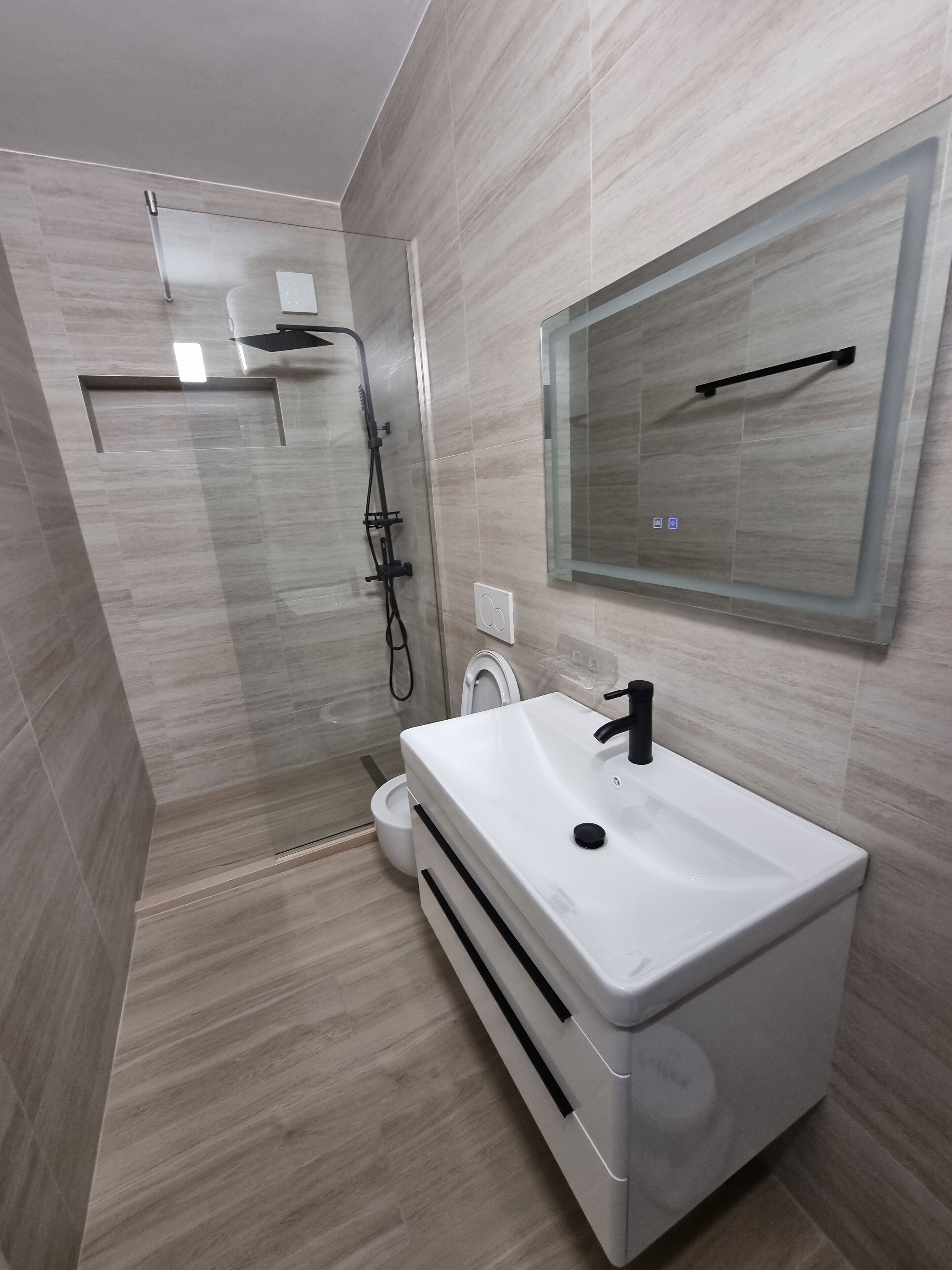 A modern bathroom with a white sink, a glass shower enclosure, and a toilet.