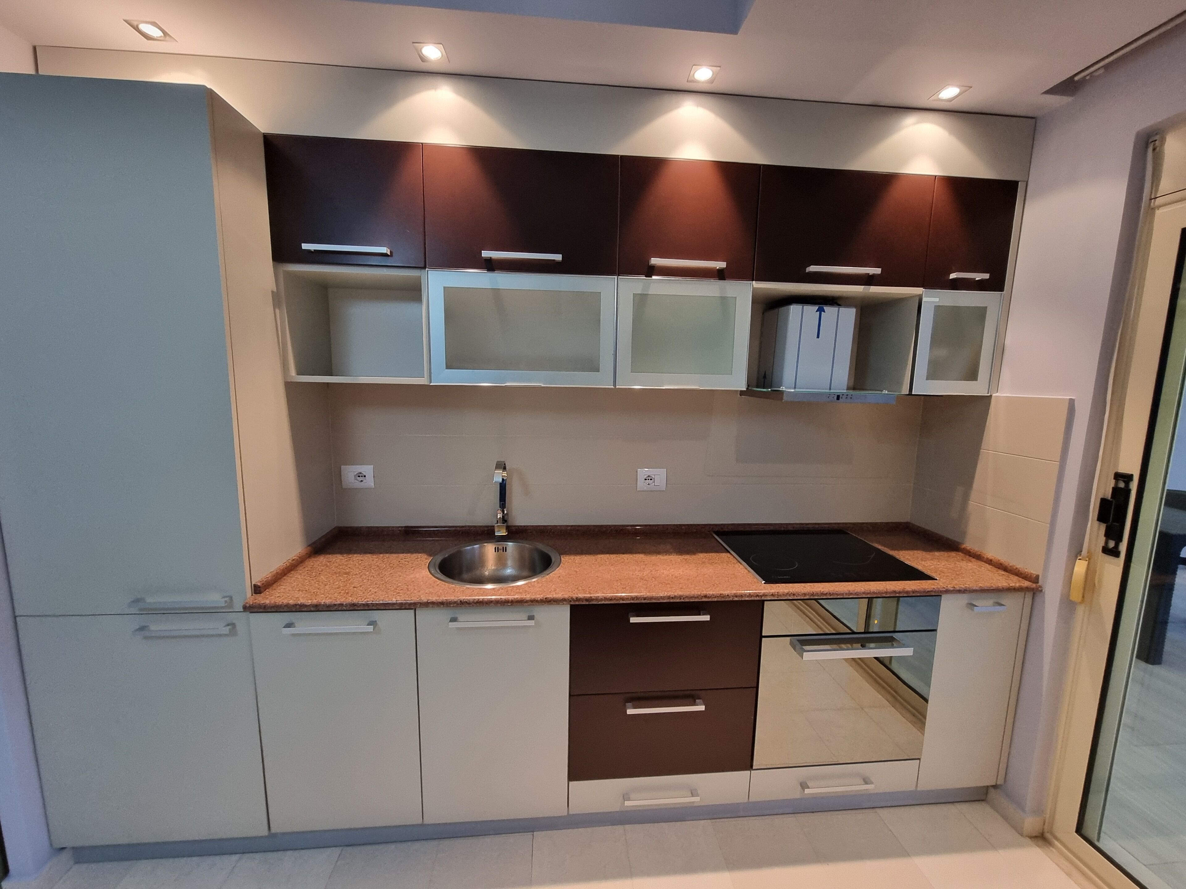 Una cocina moderna con un lavaplatos de acero inoxidable, un horno empotrado y un armario con puerta de vidrio.