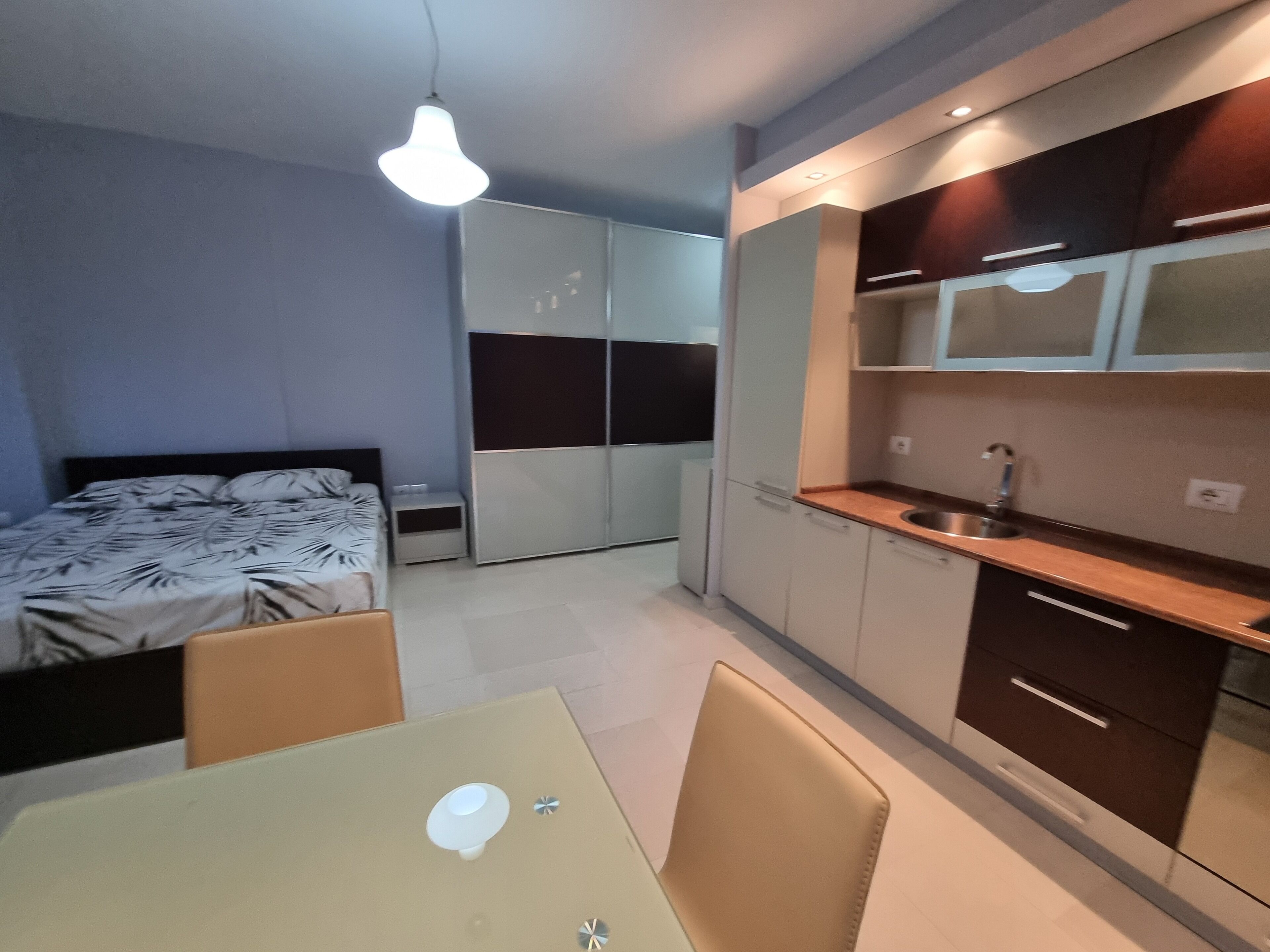 Une chambre compacte comprenant un lit, une table de chevet et une armoire. La chambre est également équipée d’une petite kitchenette avec un évier et des placards.