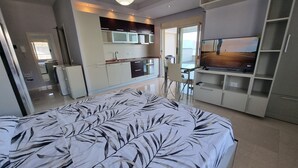 Une chambre moderne avec un grand lit, une télévision et un coin cuisine en arrière-plan.