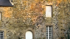 A stone building with a steeply pitched roof, two chimneys, and a small arched window with a white door. - Métairie du Hellès (Lanmeur)