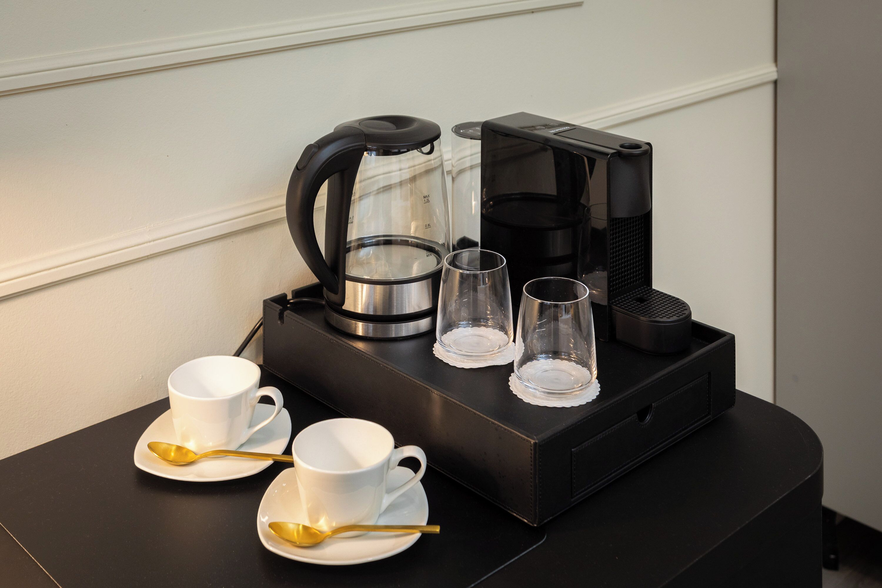 Een koffiezetapparaat, twee kopjes en twee glazen op een tafel.