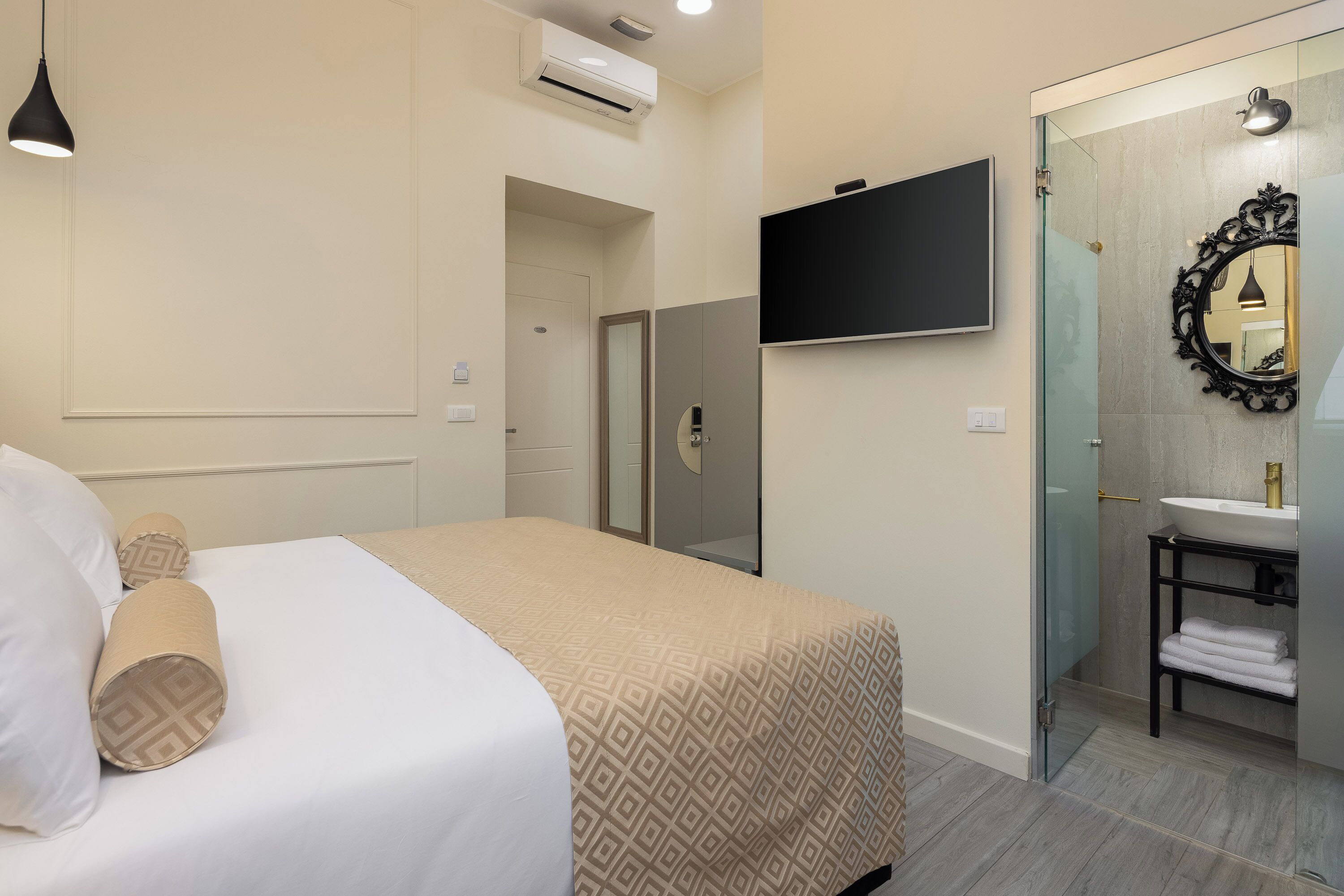 Une chambre d’hôtel comprenant un lit, un téléviseur fixé au mur, une salle de bain avec une douche à parois de verre et un lavabo avec un miroir.
