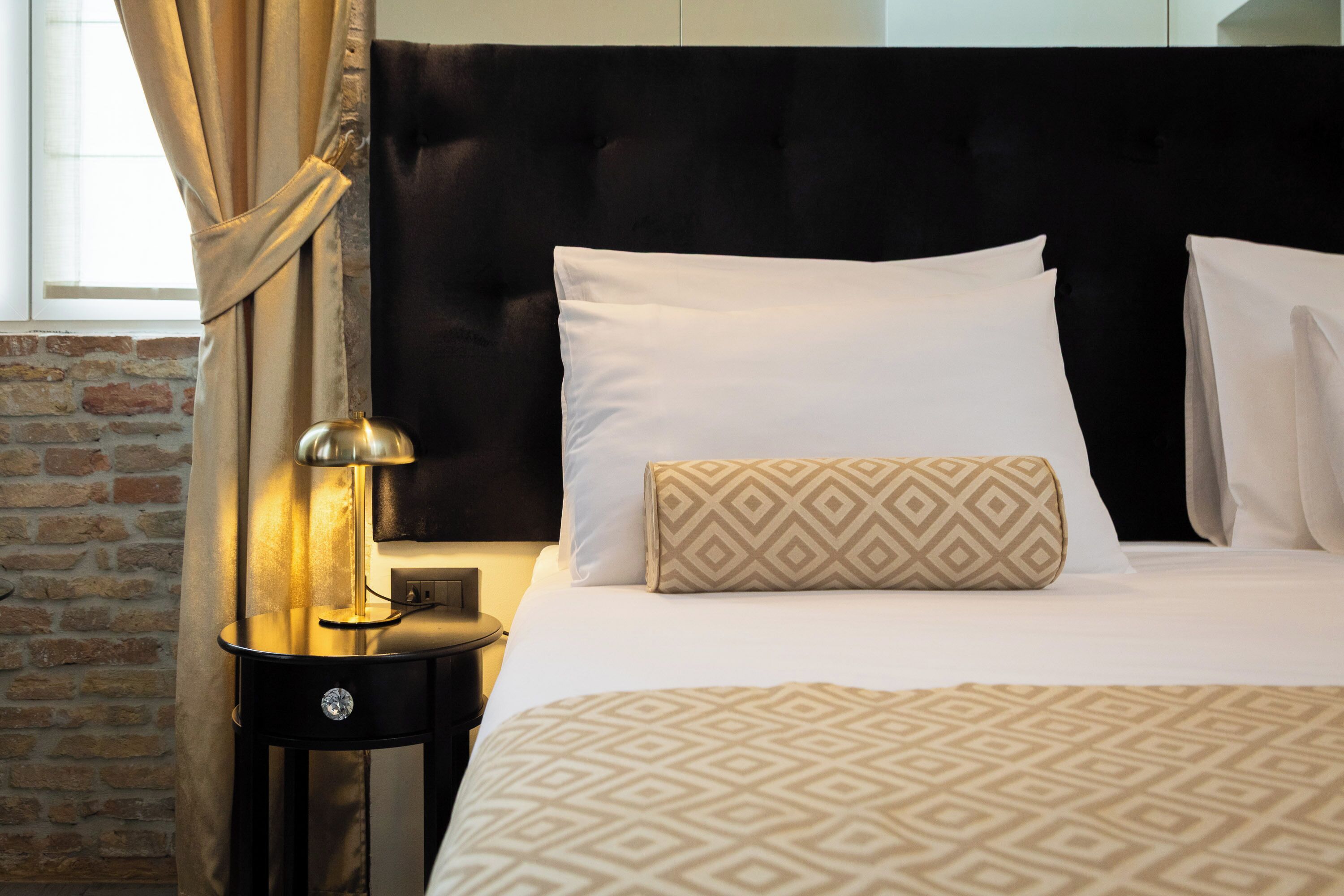 Una habitación de hotel con una cama, una mesita de noche con lámpara y una pared de ladrillo.