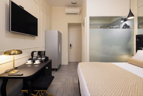 A hotel room with a bed, a desk with a coffee maker, a TV, and a shower area. - Luxury rooms Golden Palace City Centre (Split)