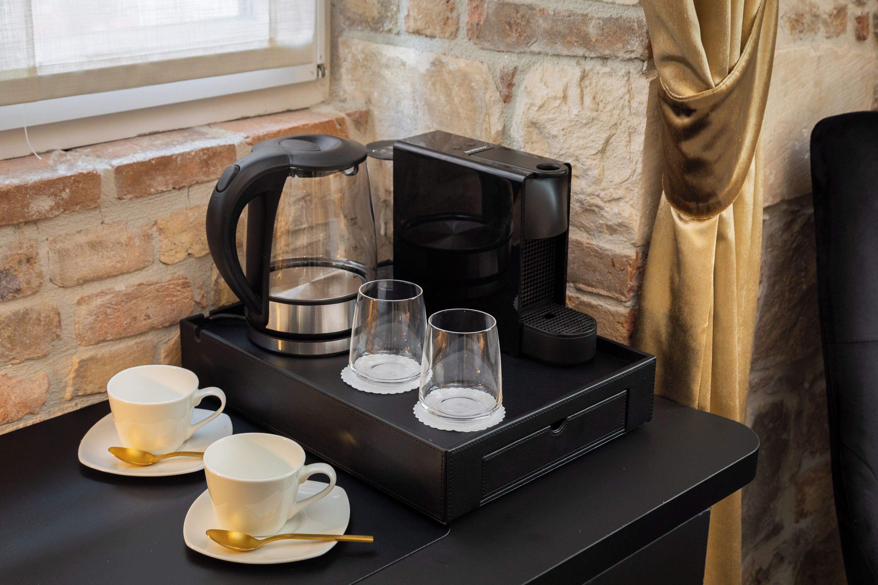A coffee station with a coffee maker, two cups, and two glasses on a black tray.