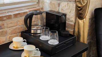 A coffee station with a coffee maker, two cups, and two glasses on a black tray.