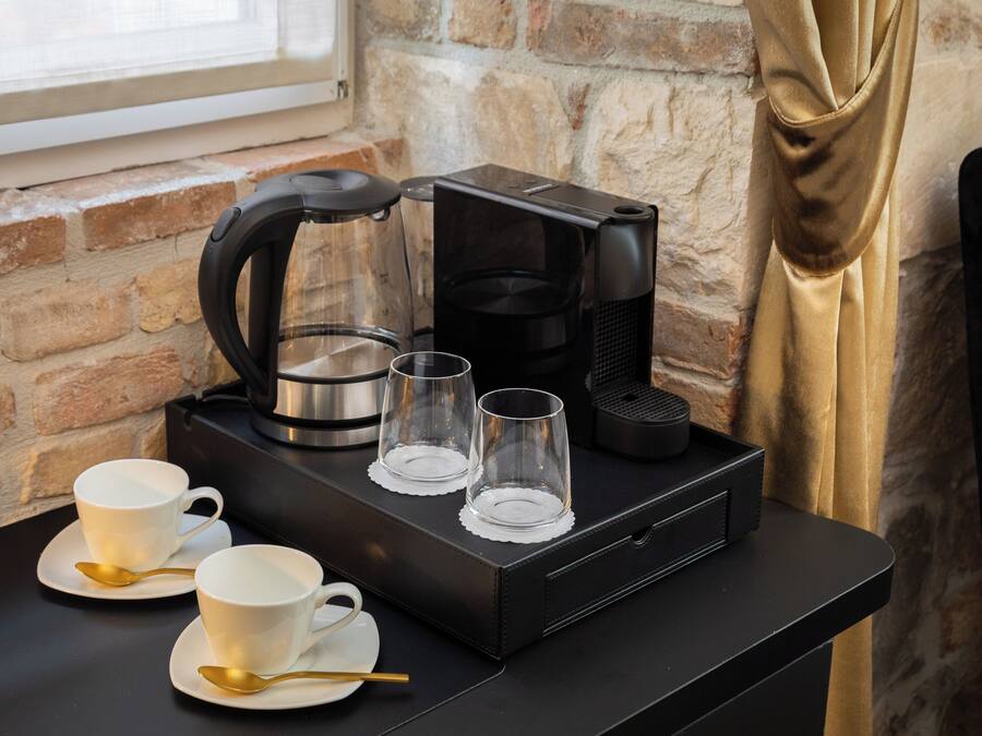 A coffee station with a coffee maker, two cups, and two glasses on a black tray.