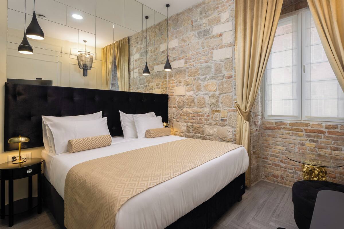 A modern bedroom with a large bed, a headboard, and a stone wall.
