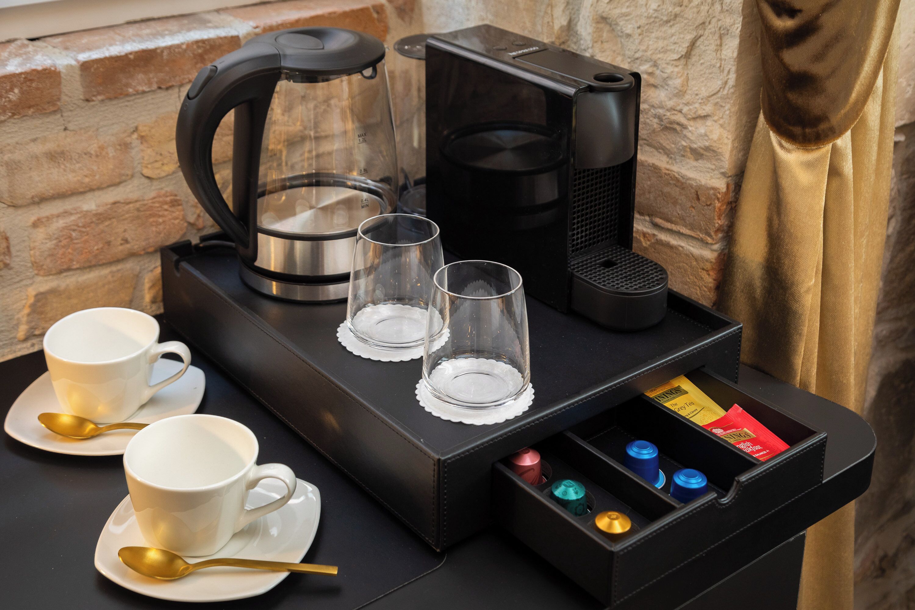 En kaffestation med to kaffemaskiner, to kopper, to glas og et rum med diverse genstande.