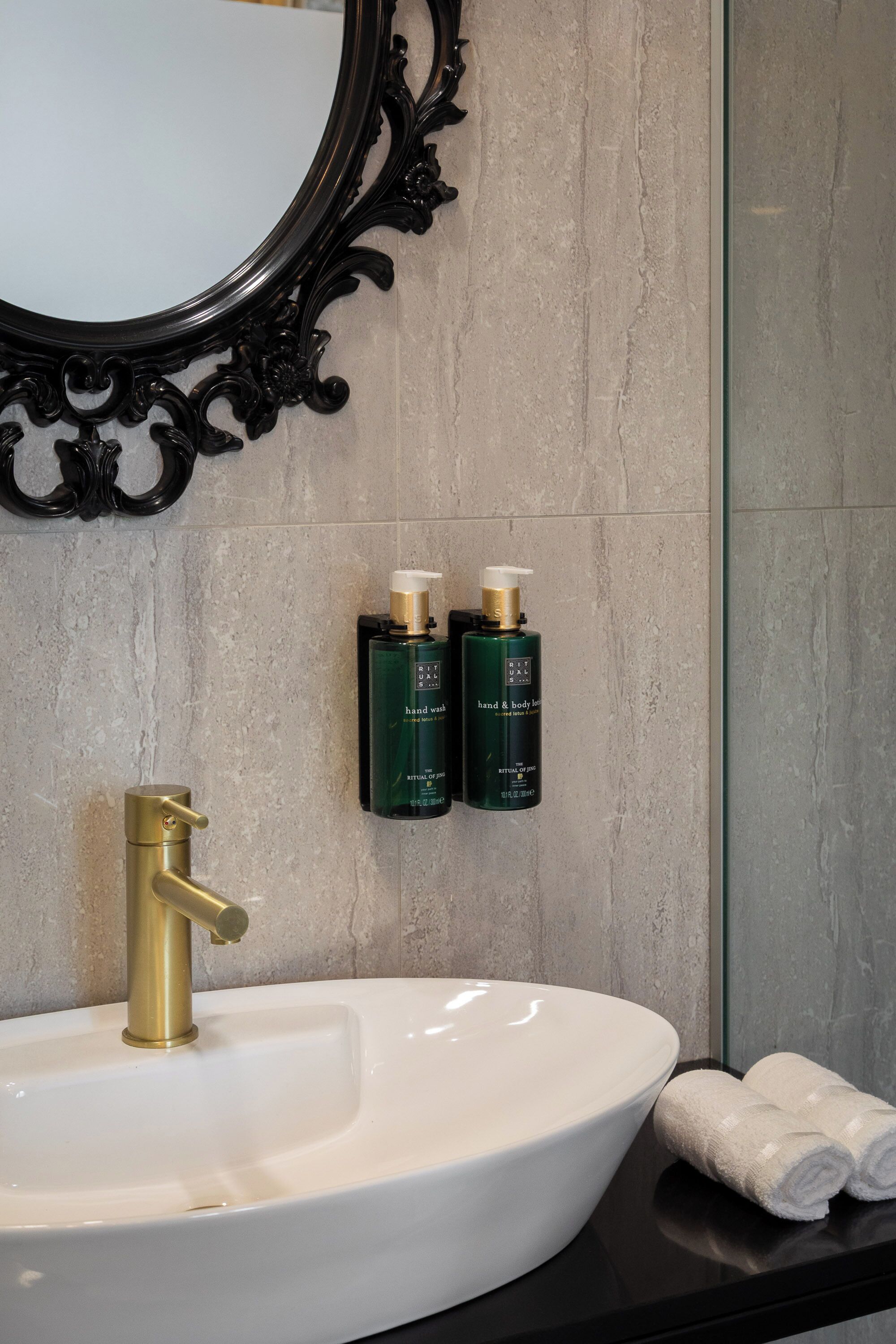 Un baño con lavamanos blanco, grifo dorado y dos botellas verdes de jabón de manos y cuerpo.