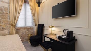 A hotel room with a bed, a desk with a coffee maker, a TV, and a black chair.